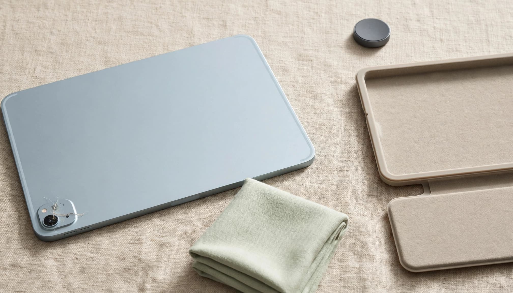 A tablet, a folded cloth, a case, and a magnetic accessory on a fabric surface.